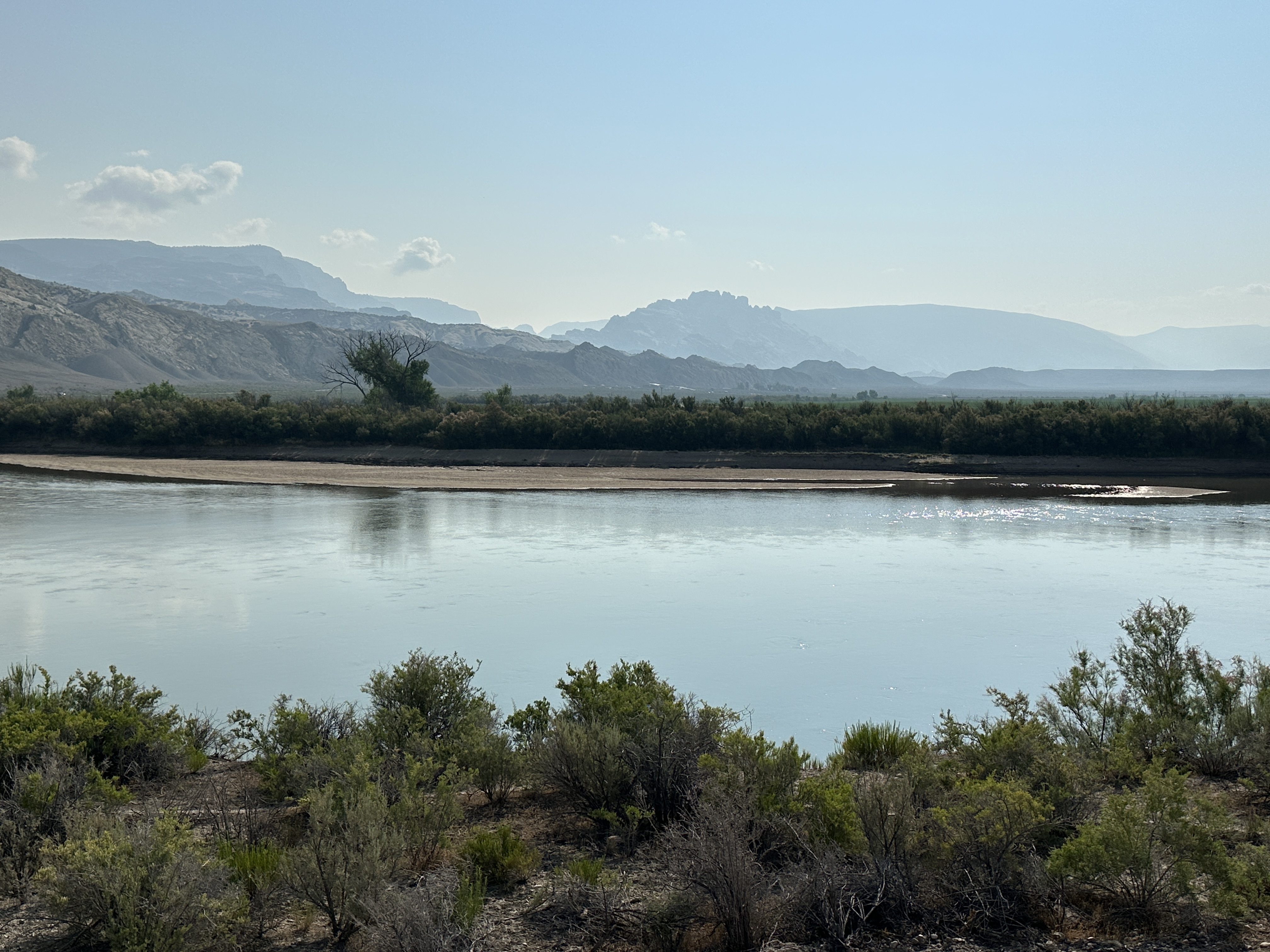 Hazy skies above rocky mountains with a river flowing in the foreground