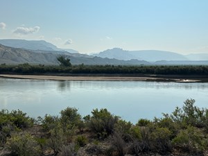 Hazy skies above rocky mountains with a river flowing in the foreground