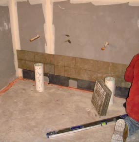 Installing tiles along the bottom of a wall in one of the bathrooms. Installing tiles along the bottom of a wall in one of the bathrooms.