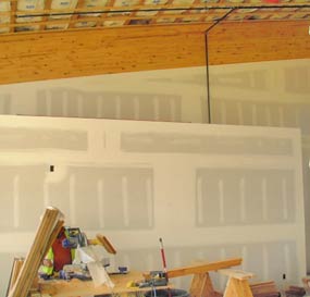 Ladder and other equipment sit in front of a wall on which the taping and mud coating of drywall has recently been completed.