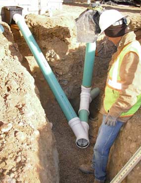 Man in a hard hat stands in dirt pit where part of a storm drain has been installed. 