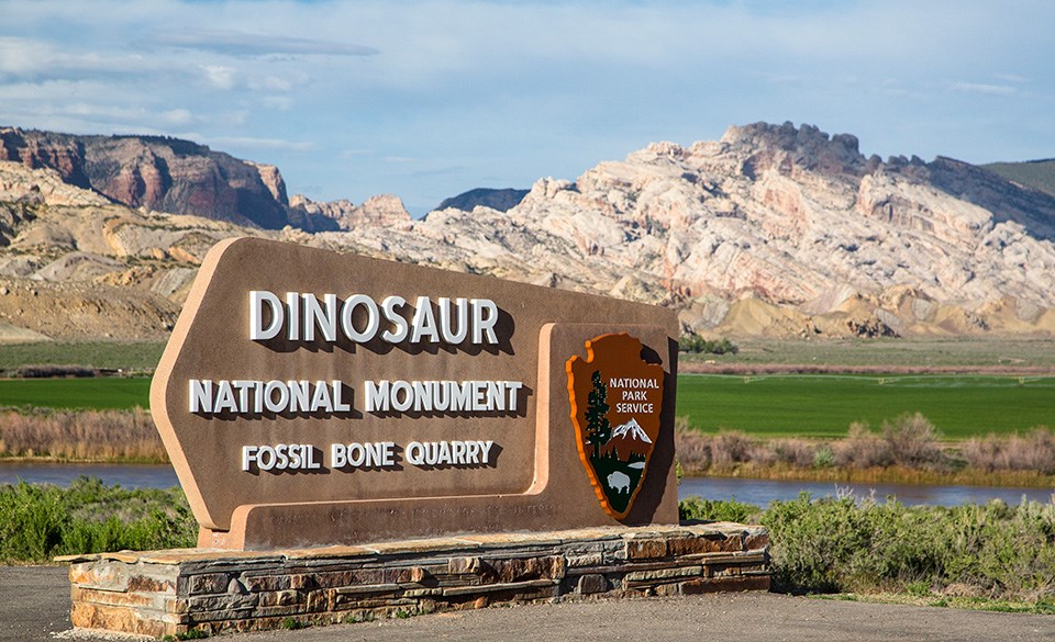 Sign greeting visitors at entrance to monument with mountains in background