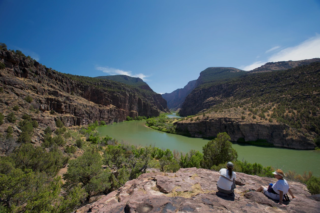 Enjoying the Gates of Lodore view Two visitors sitting on a rock looking at the view of a river flowing into a canyon.