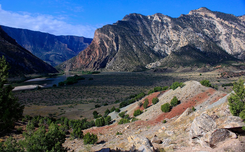 Scenic shot of hill with gray and red colored strips with rocky mountain in background.