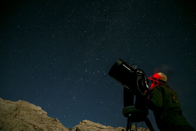 A ranger illuminated by a red light looks into a telescope.