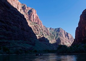 Canyon walls along the Green River dwarf a raft passing in the shadows.