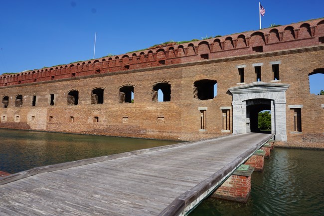 A wooden walkway over a moat leading to a brick fort