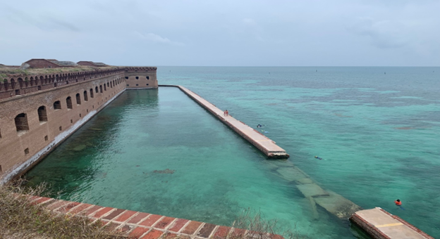 A fort surrounded by water with a broken section of the moat wall.