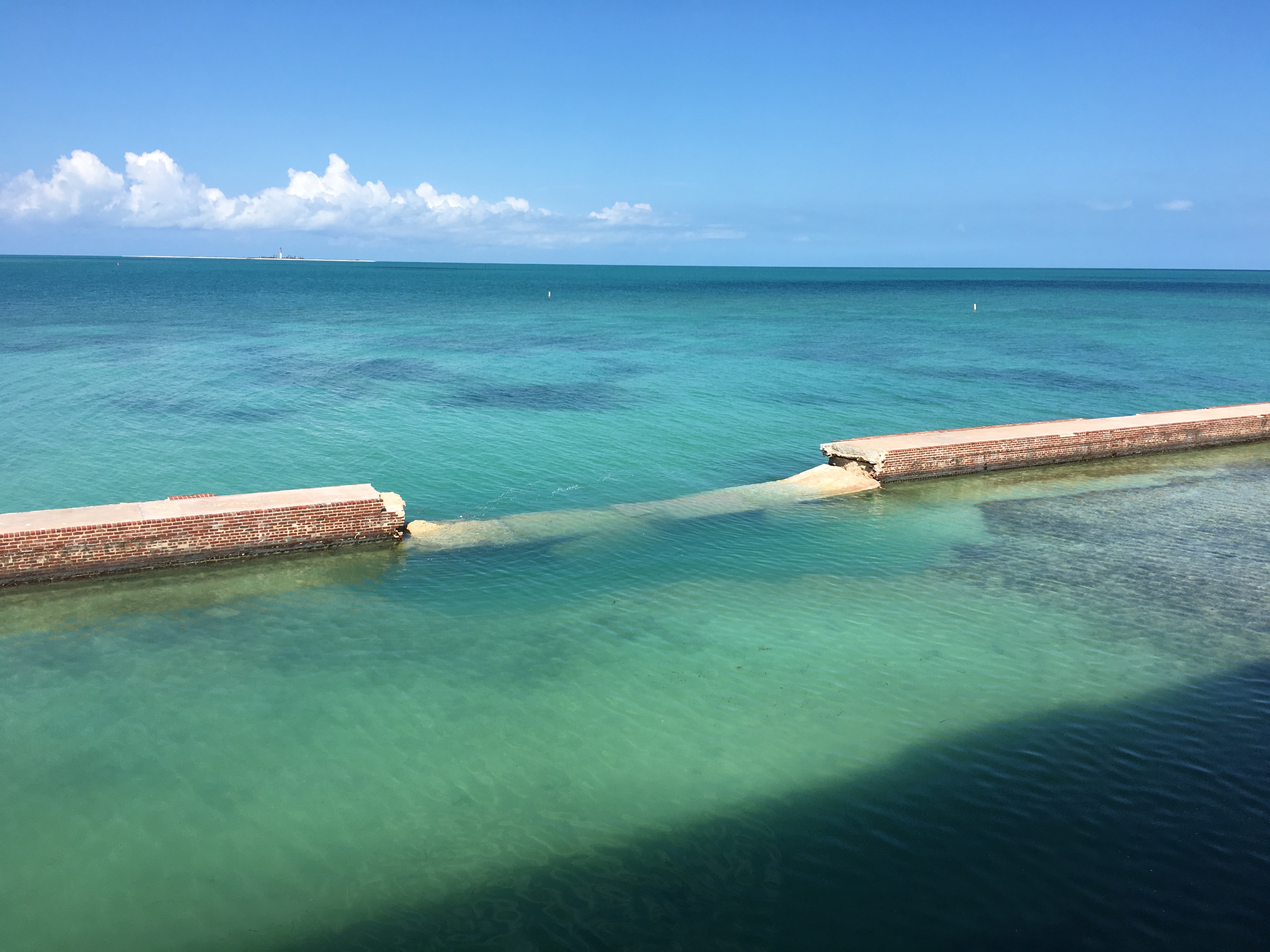 Damaged counterscarp at Fort Jefferson A wall constructed in water has a section missing allowing water to flow past over it.