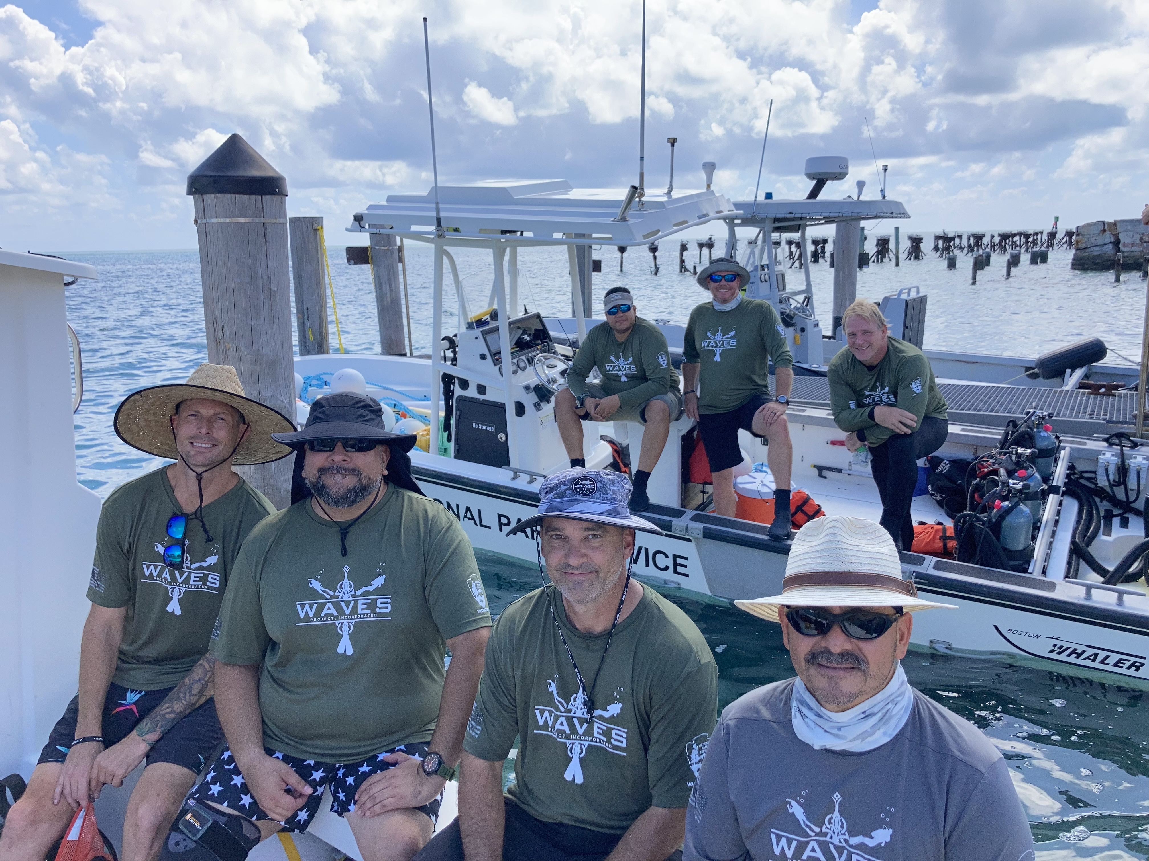 Seven men with "WAVES" t-shirts pose on boats
