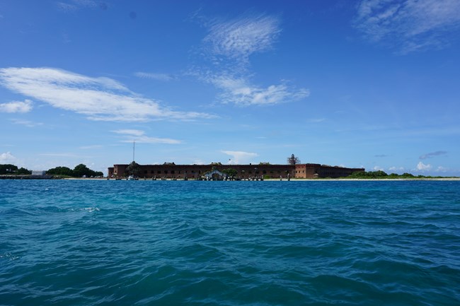 An island with a brick structure surrounded by blue ocean waters and a blue sky