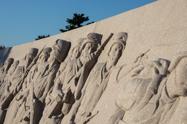 A closeup of bas relief of soldiers moving from left to right in combat gear, carrying rifles.