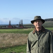 Man in hat standing in front of farm field.