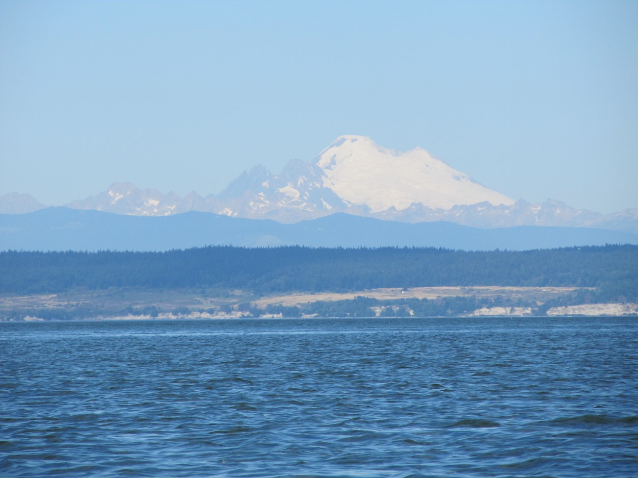 Snow covered mountain above blue ocean water.