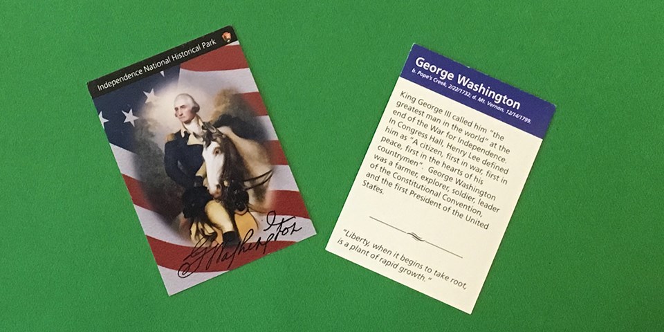 Color photo showing both sides of a trading card - one side shows a painting of George Washington on a white horse and the other side shows text about Washington's life.