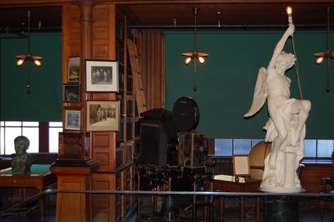 Thomas Edison's wood paneled library- three stories tall. Featuring a movie projector and statue of and angel sitting on a broken gaslight holding a light bulb.