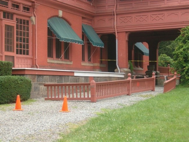 Several pieces of the dark salmon porch railing removed and sitting on the ground.