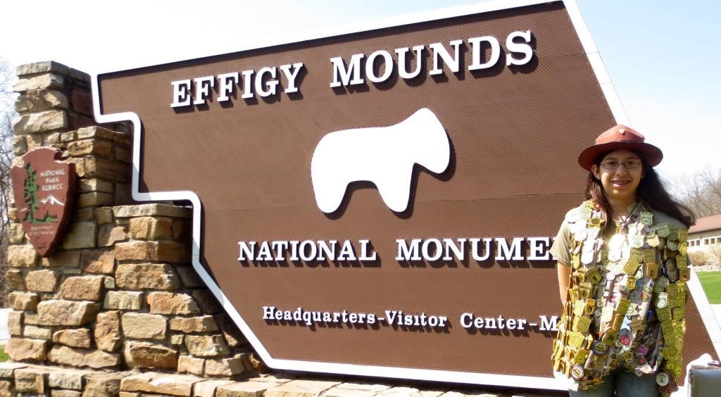 Girl standing in front of park sign with many Junior Ranger Badges.