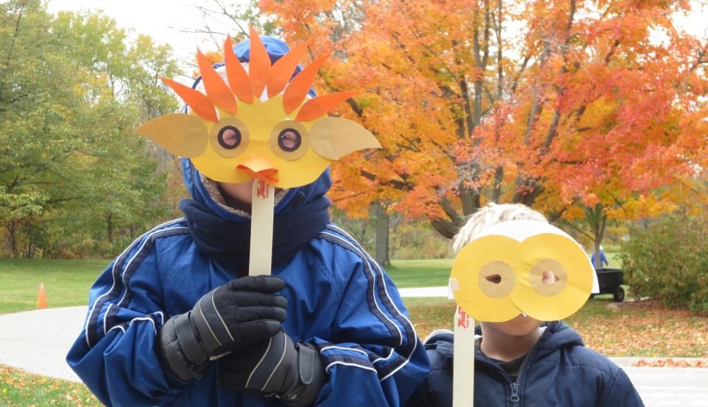 Two children holding paper masks in front of their faces.
