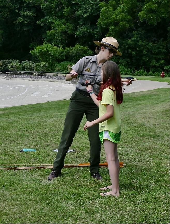 Ranger showing little girl how to hold the atlatl.
