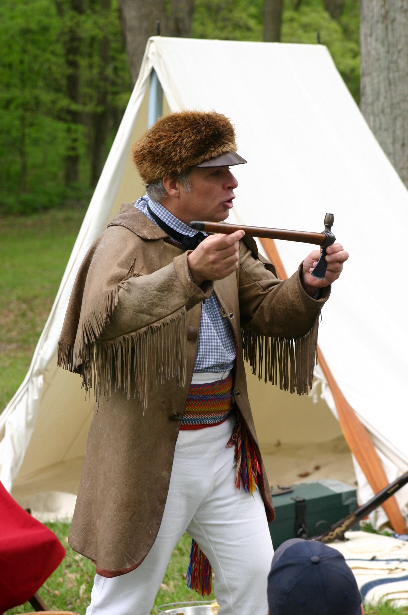 Man dressed in fur trade clothes with peace pipe in his hands talks to a crowd.