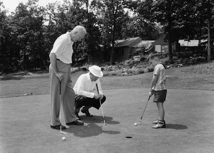 Dwight, John, and David Eisenhower stand on a putting green, playing golf