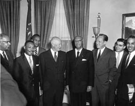 President Eisenhower stands in center, smiling, and posing with seven leaders of the African American community. E. Frederic Morrow stands in the rear in front of curtains, while Martin Luther King, Jr., stands second from left. 