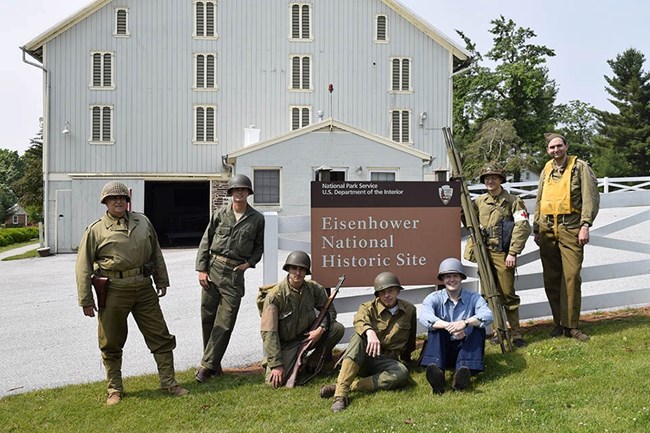 A color image showing WWII reenactors standing next to the sign for Eisenhower National Historic Site