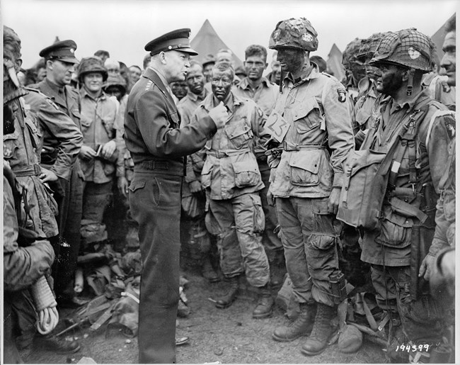 A black and white image of General Eisenhower speaking to a crowd of paratroopers