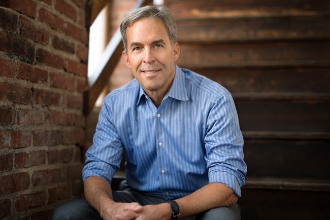 An image of a man in a button down shirt smiling at the camera