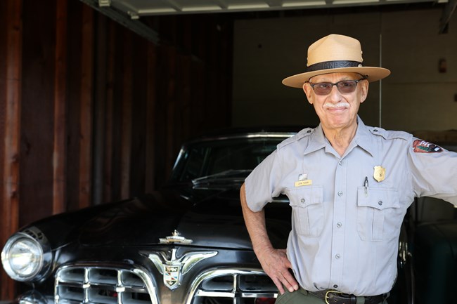 A park ranger stands in front of a historic vehicle