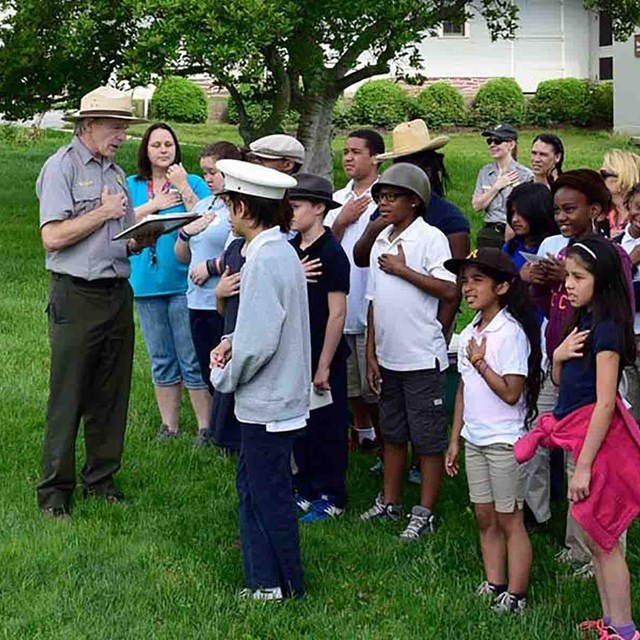A Park Ranger dressed in green trousers, grey shirt, and tan hat, speaks to a group of children at the Eisenhower National Historic Site