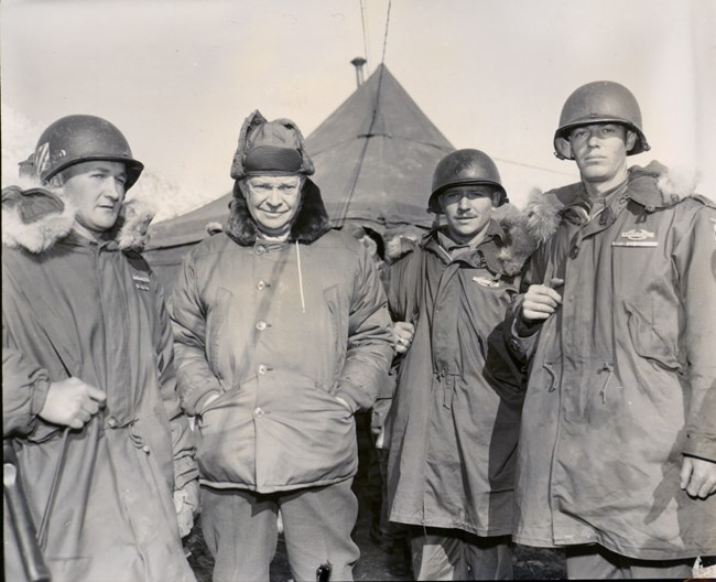 A black and white image of Dwight Eisenhower wearing a heavy winter parka standing with several soldiers in Korea