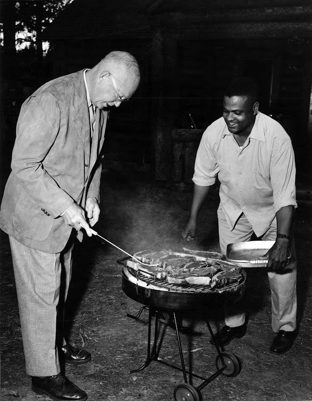 With John Moaney looking on, smiling, President Eisenhower cooks up some food on a grill