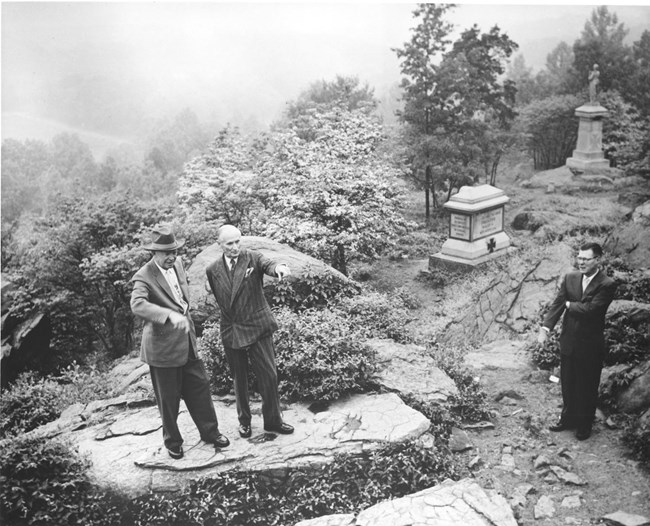 Dwight Eisenhower and Bernard Montgomery stand atop large rocks on Little Round Top while touring the Gettysburg battlefield. In the background are several monuments.