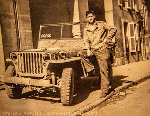 A black and white photo of Paul C. Martz with his Jeep parked along a street in France.
