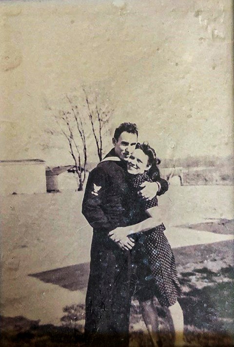 A black and white photo of Page Evans in his military uniform hugging a woman in a yard with a tree in the distance.