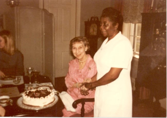 Mamie Eisenhower is seated; standing next to her is Delores Moaney. On a table in front of Mamie is a cake.