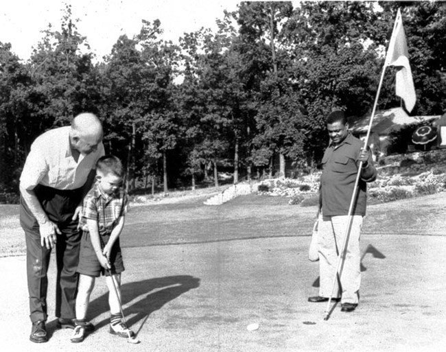 Dwight and David Eisenhower Putting With Moaney Nearby President Eisenhower helps Grandson David put a golf ball; John Moaney is standing at the hole, holding a flag