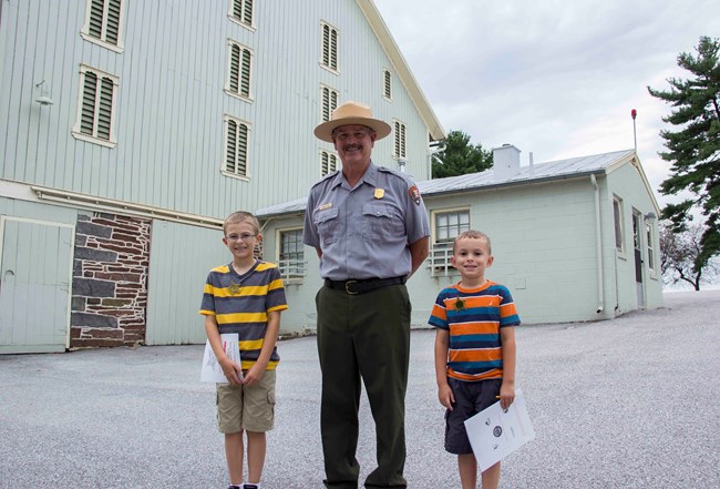 Two kids next to a ranger after completing the Junior Secret Service Program