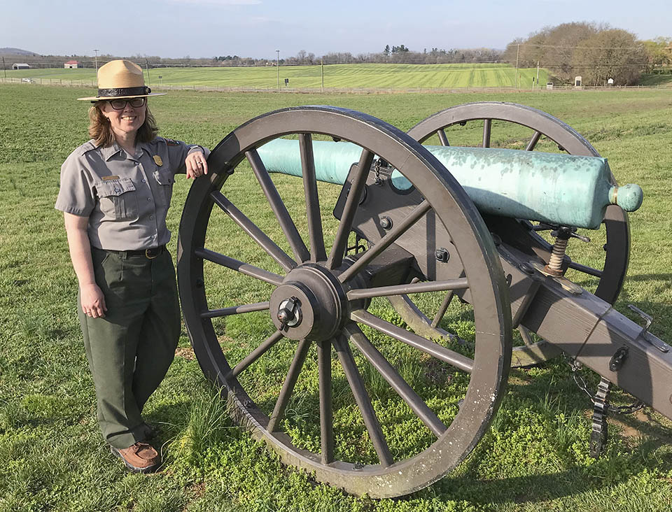 Jana Friesen McCabe Named Site Manager of Eisenhower National Historic Site. A female National Park Service ranger stands next to a Civil War cannon in an open green field.