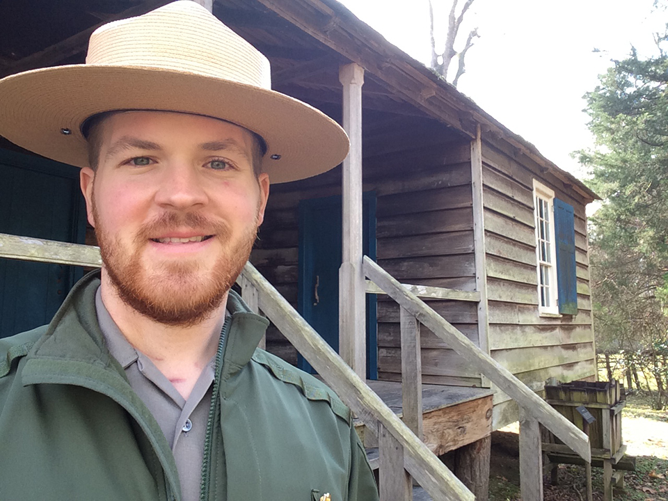 Jacob Dinkelaker has been selected to serve as the Eisenhower National Historic Site Interpretation Program Lead. He stands in uniform in front of a small wooden house.