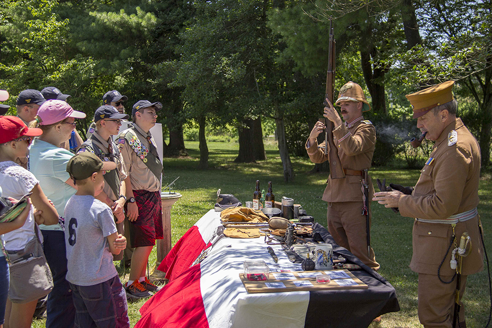 Two living historians, portraying Allied soldiers, demonstrate how to load their firearms to a group of Boy Scouts.