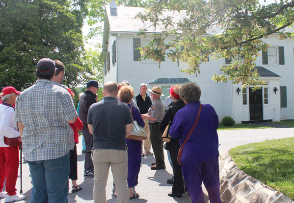 A park ranger presents an interpretive program in front of the Eisenhower home. The group is standing in a paved pathway near the front yard and the Eisenhower home is behind the group.