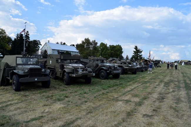 A row of dark green WWII era jeeps in a field