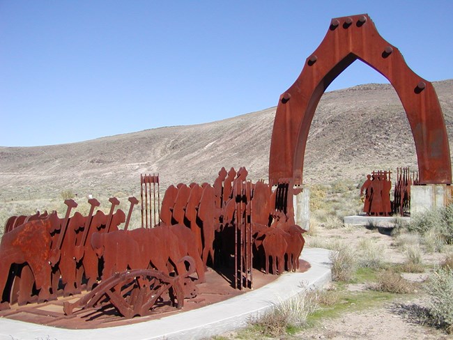 A statue of people walkin through an arch, in a desert setting.