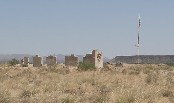 ruins of a fort with an American flag beside the ruins and a black mesa in the background ruins of a fort with an American flag beside the ruins and a black mesa in the background