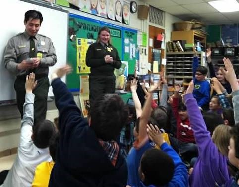 Park rangers in front of a 4th grade classroom with kids eagerly raising their hands.