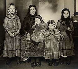 Woman seated holding infant surrounded by three standing girls