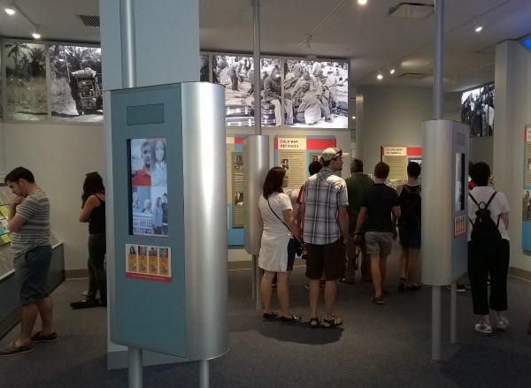 Visitors in New Eras Gallery looking at exhibit text, watching video, and listening to audio.